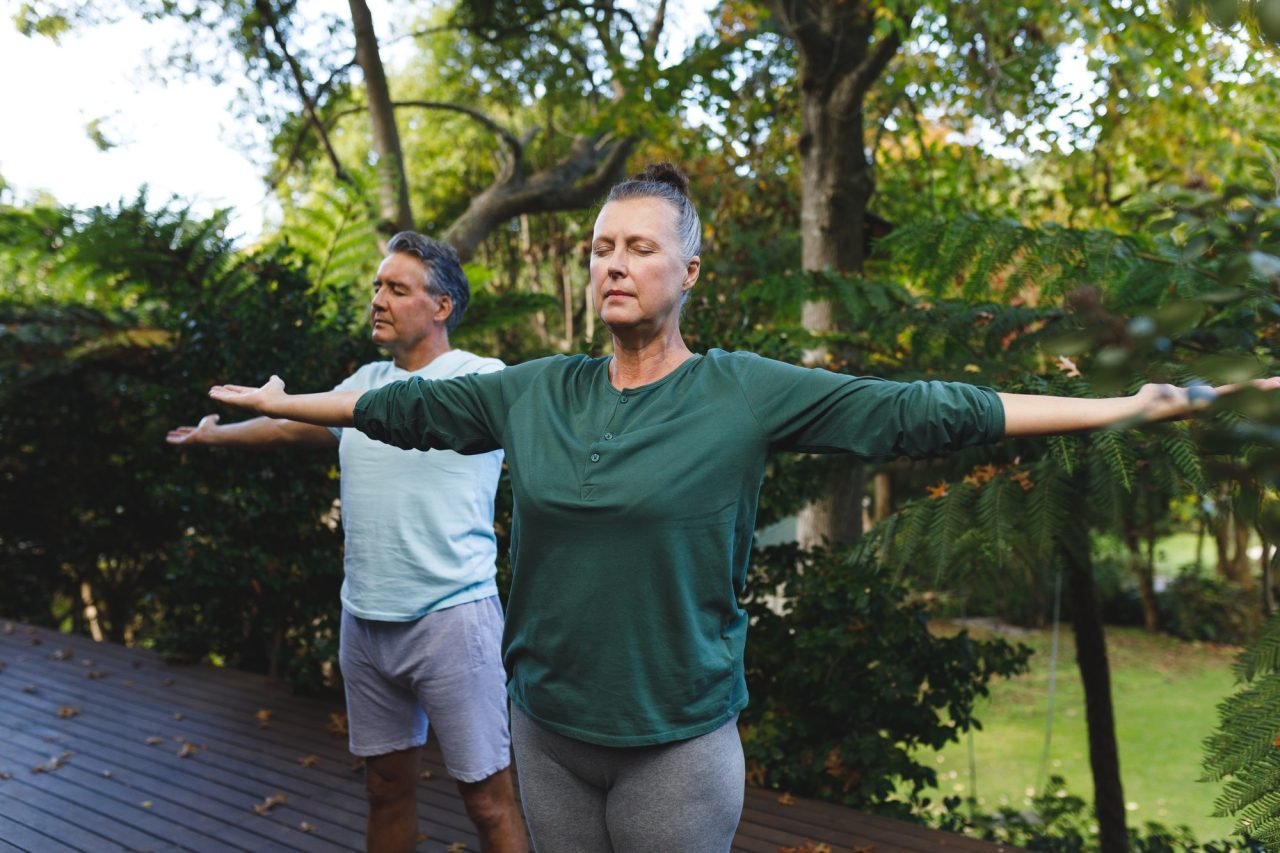 Happy senior caucasian couple practicing yoga, stretching in sunny garden